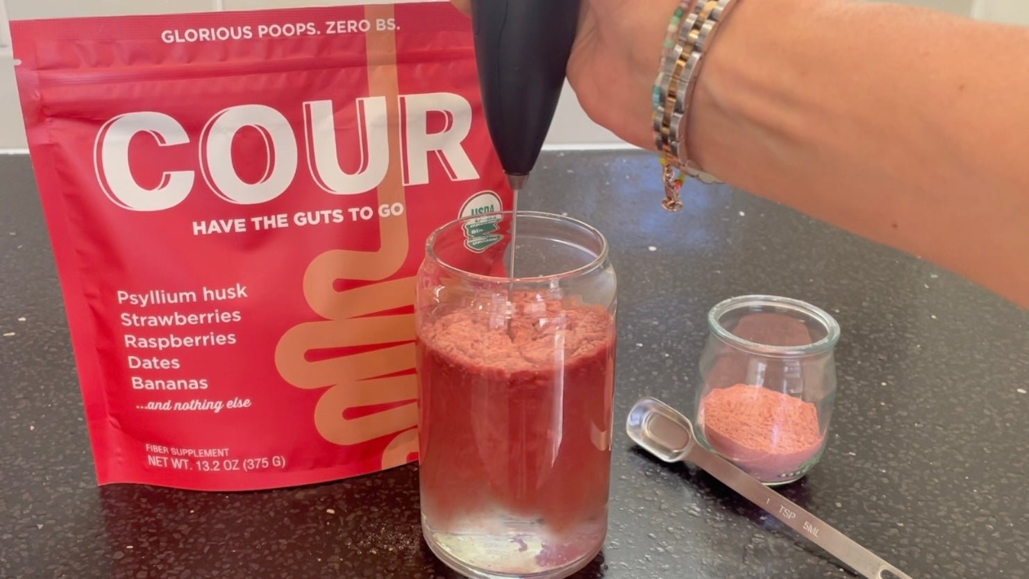 Pouring Cour, a red powder, into a glass of water then mixing it with a milk frother